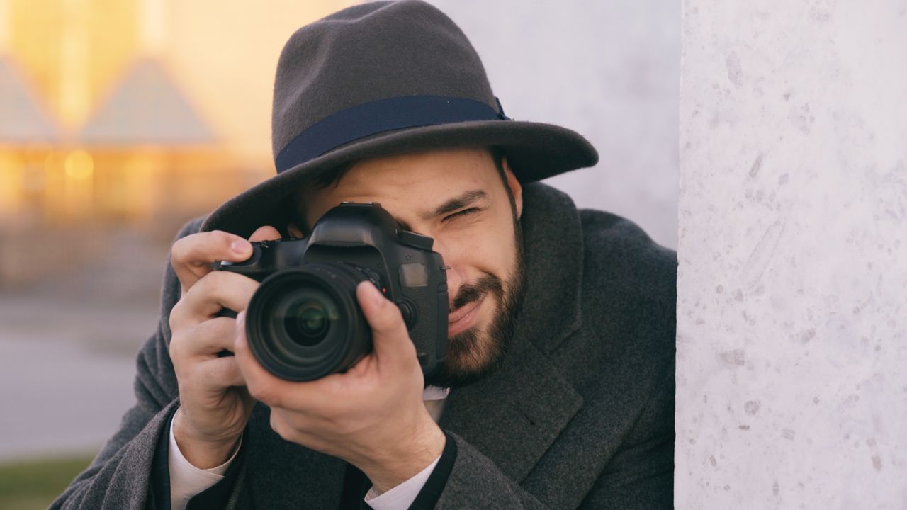Bearded man with hat and camera taking photos outdoors, focused and artistic.