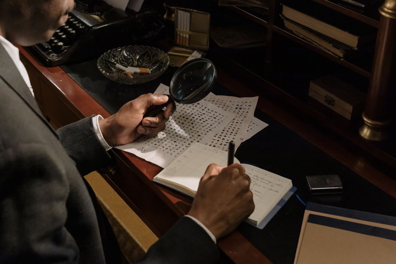 Detective using magnifying glass to analyze cryptic documents in vintage office setting.